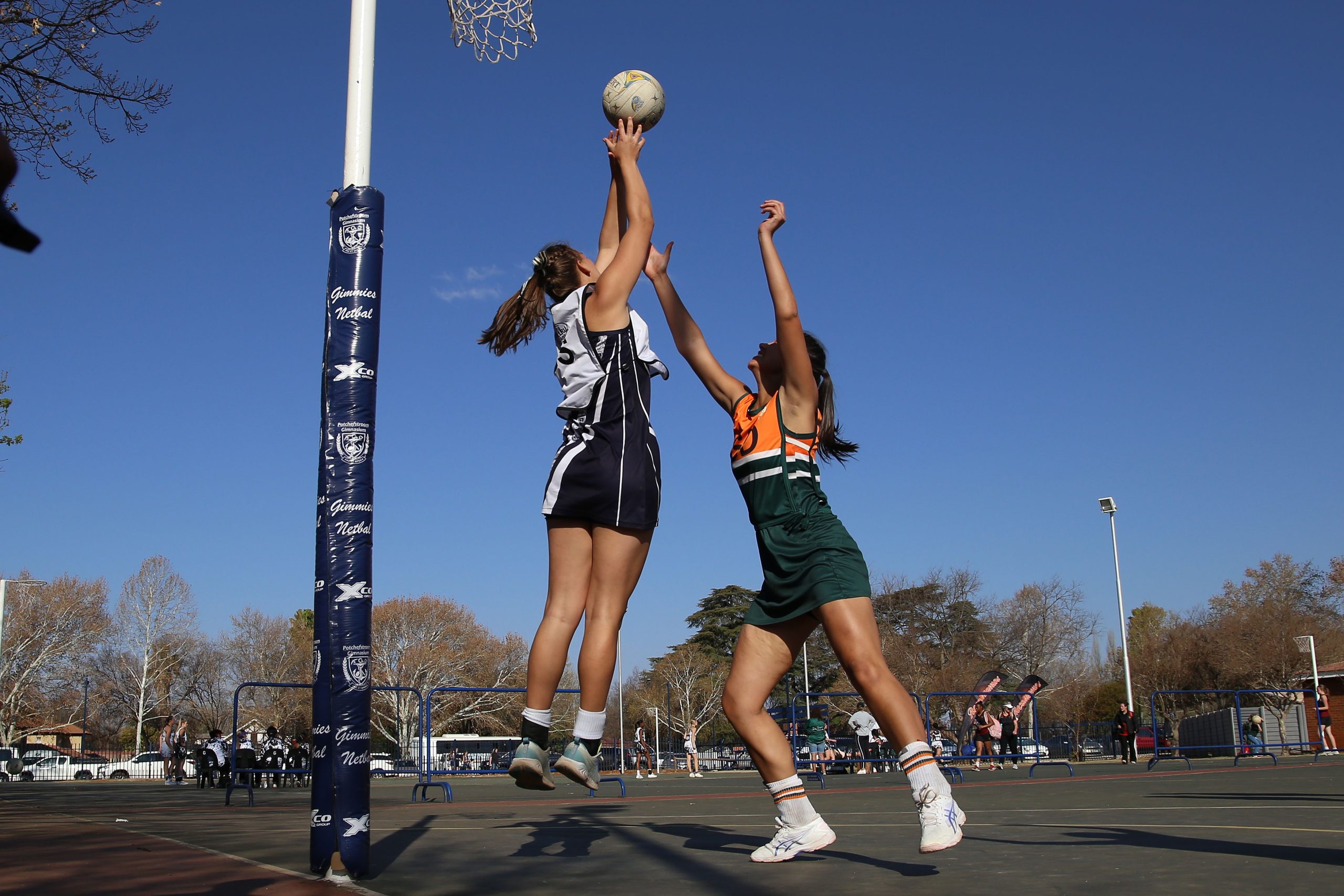 Two female netball players in action on an outdoor court during a sunny day.